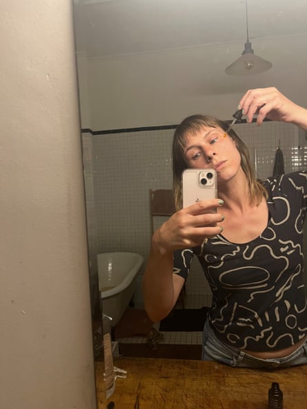 一位女士站在镜子前,涂睫毛膏并用智能手机拍摄