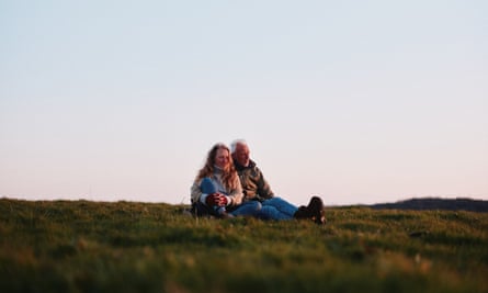 The writer, Raynor Winn, left, and her husband taking in the landscape of the Isles of Scilly while sat on a grassy hill at dusk.