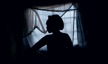 Photograph of a woman in silhouette against the window of a shack in South Africa