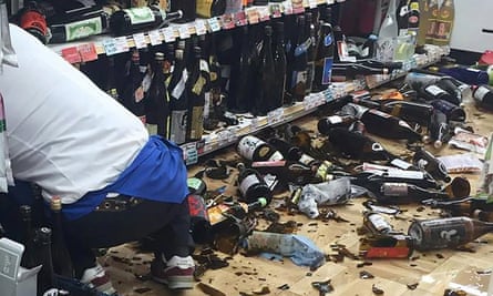 A shop clerk cleans broken wine bottles after the quake.