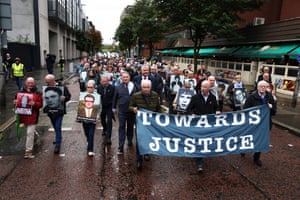 A group of people walks along a road carrying a banner that reads ‘towards justice’