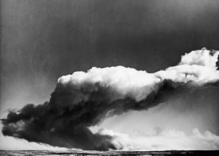 A huge cloud of smoke billows over the sea in a black and white photo.