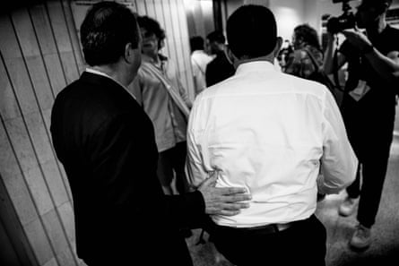A man in a suit walks with another man toward the elevator