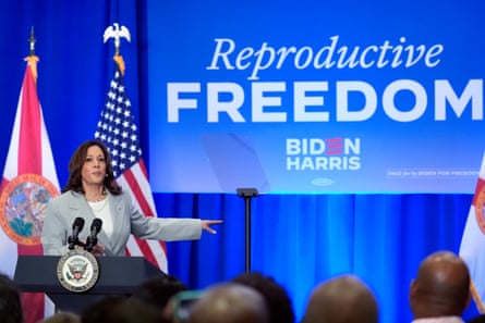 Woman wearing grey suit stands at podium and points to screen