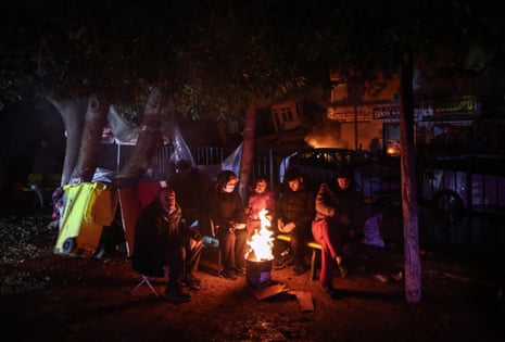 People warm themselves up around a fire as emergency personnel search for victims at the site of a collapsed building after an earthquake in Iskenderun district of Hatay, Turkey, 06 February 2023.