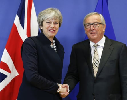A woman in a navy-blue suit shaking hands with a man with grey hair wearing a grey suit and a Burberry tie