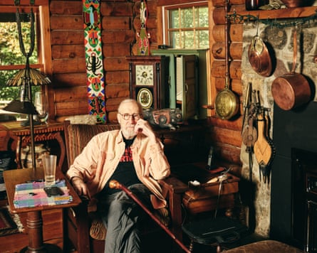 James Cromwell sitting surrounded by his stuff in his log cabin