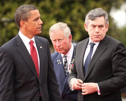 Barack Obama looks towards Gordon Brown who looks away as then Prince Charles peers between them to camera. All look sombre