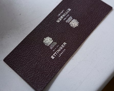 A dark leather tag with silver embossed logos reading “Ettinger London” lies on a white surface