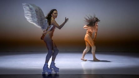 Two partially nude female dancers on a spotlit stage, one of them wearing angel wings and roller skating, the other thrashing with her hair awry.