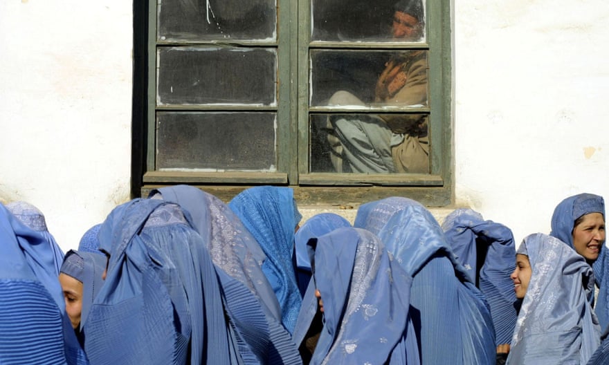 In February 2002, a man looks at Afghan women waiting to apply for jobs at Kabul’s Ministry of Women, which initiated a drive to encourage professional women to re-enter the workforce after the demise of the Taliban.