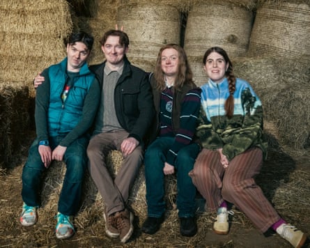 Four people sit on hay bales in a barn, smiling at the camera