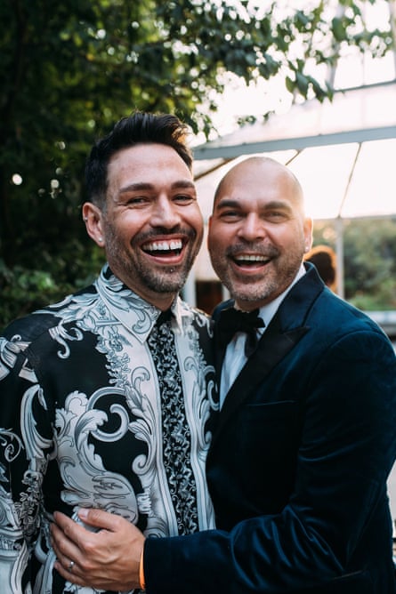 Dion Padan and Ben Graetz at their first wedding anniversary. Dion is wearing a paisley black and white button shirt, and Ben is wearing a dark navy suit with a bow tie. They look extremely happy.