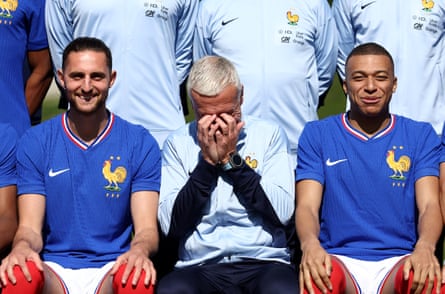 Adrien Rabiot and Kylian Mbappé smile, sat either side of Didier Deschamps who covers his face with his hands