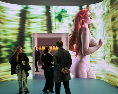 People look at a large screen showing a naked woman walking past blurred trees