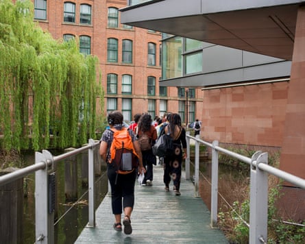 A view from behind a walking tour group as they cross a narrow wooden footbridge with silver safety railings.