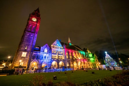 A large Victorian town hall at night, illuminated in primary colours, with a Christmas tree on a green in front.