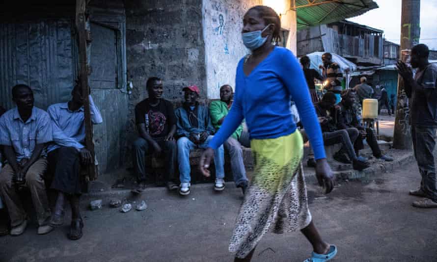 woman in mask walking down street watched by a group of men