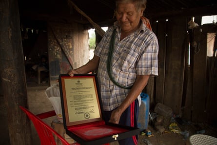 An old man in a hut shows off a brass plaque