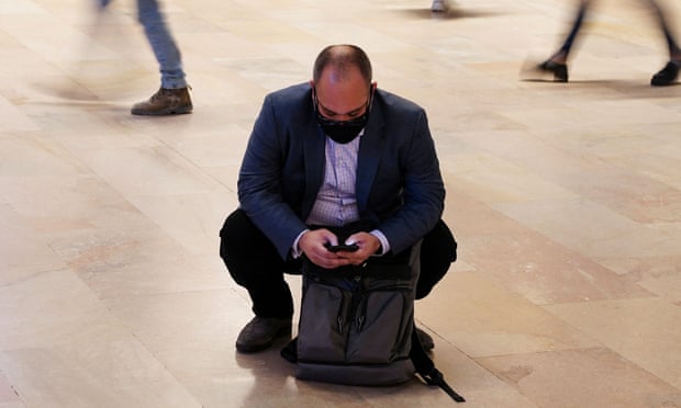 A person wearing a mask squats to check his phone in Grand Central Terminal in New York City. 
