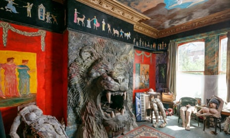 A room with a large lion's head sculpted around a fireplace with paintings of people on the wall either side and stuffed bodies, torsos and legs of human-sized dolls sitting on chairs