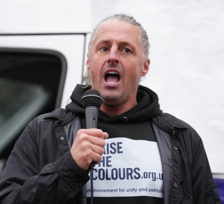 Ryan Bridge, wearing a ‘Raise the Colours’ hoodie, speaks into a microphone.