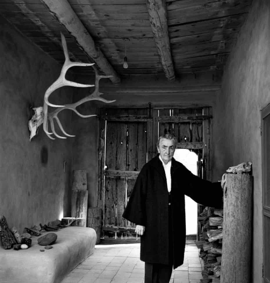 Georgia O’Keeffe  in 1967 at the entrance of her New Mexico home, wearing a big coat, with an elk horn hanging on the wall and bones on a shelf