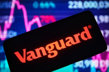 The Vanguard Group logo on a smartphone screen and a stock market line graph is in the background.