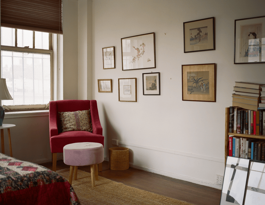 A view of a bedroom with a red velvet chair and drawings on the wall