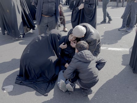 Woman sat on ground apparently being comforted by another woman, a man and a child.