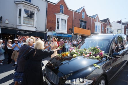 Two older women throwing flowers on the hood of the hearse