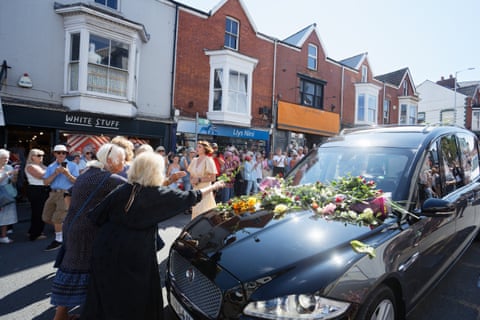 Two older women throwing flowers on the hood of the hearse