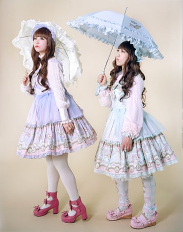 Two women in pastel lace dresses hold ornate ruffled parasols, looking off to the side