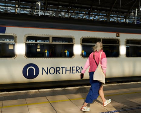 A woman with a shoulder bag walks along a platform past a Northern train
