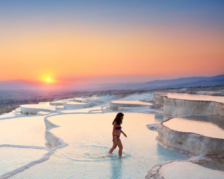 A woman in a bikini standing in one of a series of rock pools on a hillside at sunset