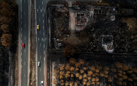 Motorists drive past homes destroyed and woodland burnt in wildfires