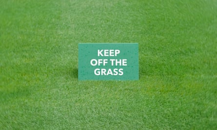 A keep off the grass sign in the middle of a dark green lawn