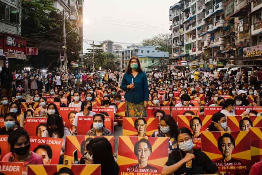 Protesters with placards showing the image of detained Myanmar civilian leader Aung San Suu Kyi sit along a street before holding a candlelight vigil during a demonstration against the military coup in Yangon