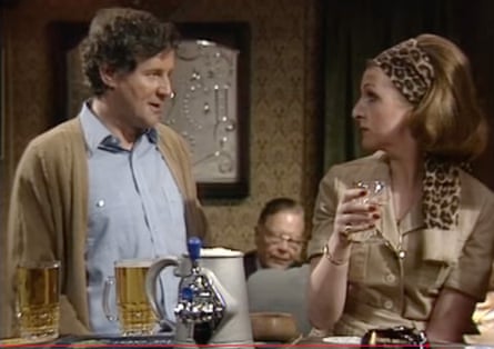 A man in brown cardi and woman in safari style shirt and leopard print head scarf/ band
