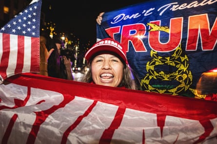 A woman in a Trump hat smiles and waves a Trump banner.