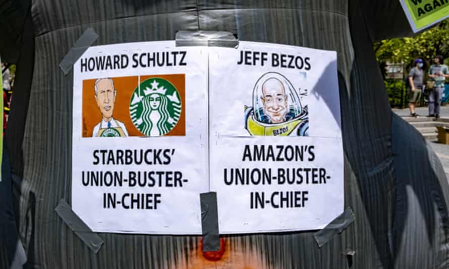 signs read: 'howard schultz, starbucks' union-buster-in-chief' and 'Jeff Bezos, Amazon's union-buster-in-chief'