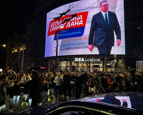 Crowds gather at night in Belgrade before a large screen showing election imagery