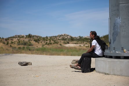 A man sits at the base of a metal support structure in the hot sun.