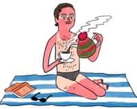 A sunburned man in swim trunks sits on a beach towel, pouring tea from a kettle wearing a knitted hat