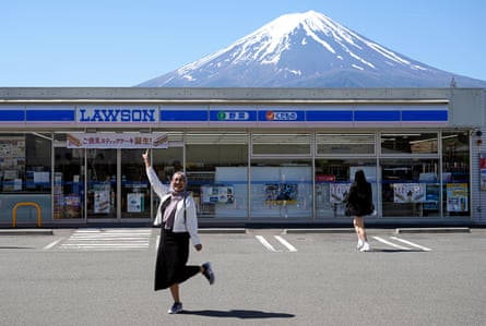 A tourist poses in front of a convenience store with Mount Fuji seen in the background, in Fujikawaguchiko, north of Mount Fuji, Japan.