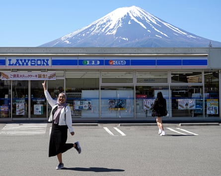 A tourist poses in front of a convenience store with Mount Fuji in the background