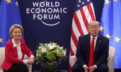 A man and a woman sit in front of a World Economic Forum sign and a US flag.