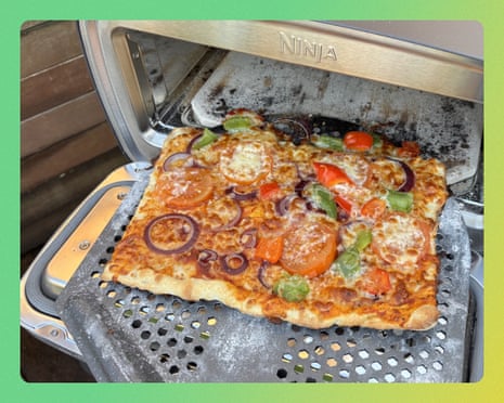 A rectangular pizza topped with tomatoes, onions, peppers, and cheese sits in a Ninja pizza oven