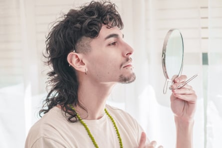 young man with mullet looks in a mirror