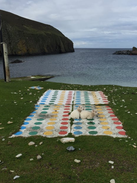Photograph of two sheep sitting on a game of Twister by the sea